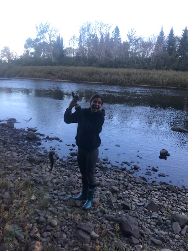An excited woman holds up a fish she caught next to a river in Maine.